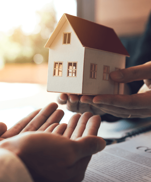 a person handing over a wooden replica home