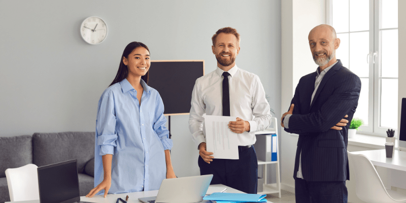 3 business professionals smiling behind a desk