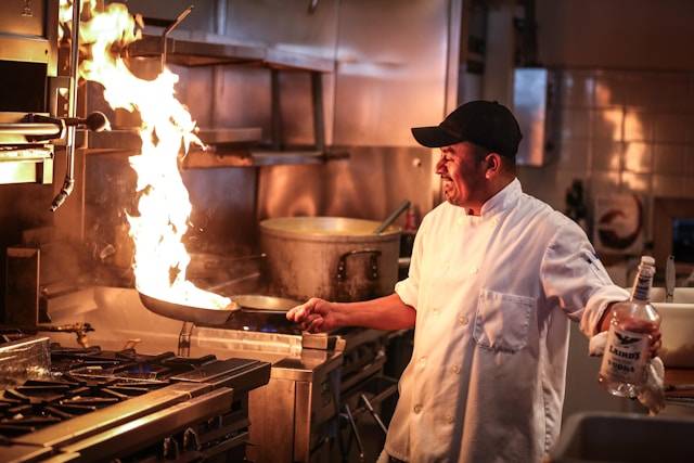 A chef cooking on a stovetop with a large fire