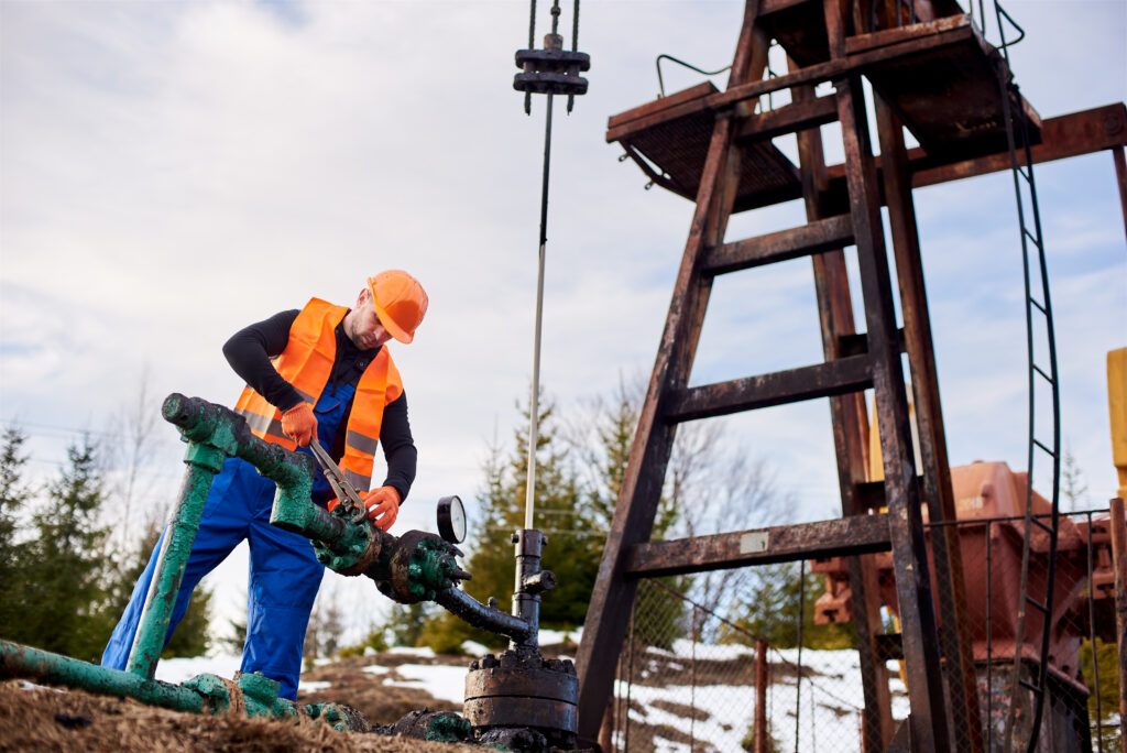 oil worker orange uniform helmet working with pipe wrench near oil pump jack